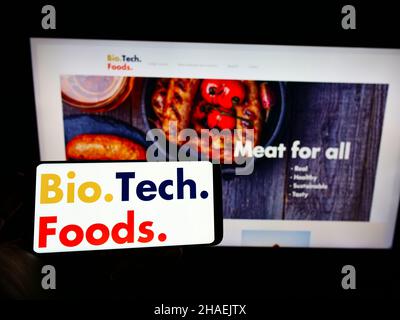 Personne tenant un smartphone avec le logo de la société espagnole de viande de culture BioTech Foods sur l'écran devant le site Web.Mise au point sur l'affichage du téléphone. Banque D'Images