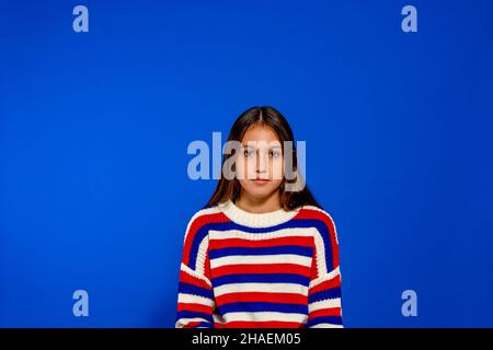 Adorable jeune femme hispanique vêtue de chandail rayé pose pour le portrait avant isolé sur fond bleu studio Banque D'Images