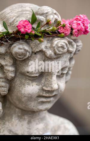 Tête d'une figurine d'ange avec une couronne de fleurs roses roses Banque D'Images