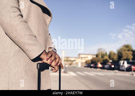 détail des mains d'une femme d'affaires dans la valise qui attend un véhicule sur la route Banque D'Images