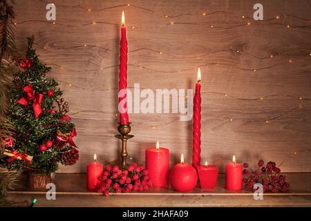 Carte de Noël avec un arbre, des bougies et des guirlandes brillantes.Des bougies rouges brillantes brûlent sur l'étagère de la cheminée près de l'arbre de Noël A. Banque D'Images