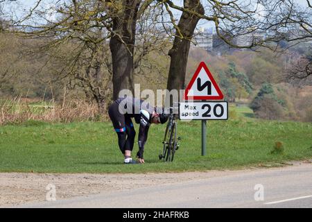 Londres, Angleterre - avril 17 2018 : cycliste de sexe masculin s'étendant à côté d'un panneau de vitesse à Richmond Park, Londres Banque D'Images