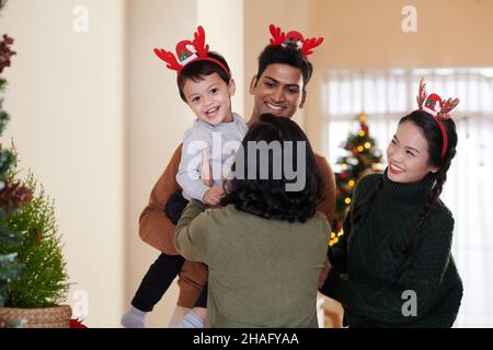 Parents donnant un petit fils excité à une grand-mère heureuse qui est venue pour des vacances de Noël Banque D'Images