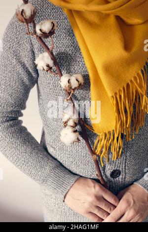 Un homme dans un gilet gris et une écharpe brillante est debout avec une branche de coton sur un fond clair.Vue avant. Banque D'Images