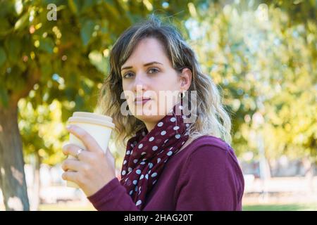 Femme blonde tenant un café à emporter dans un parc Banque D'Images