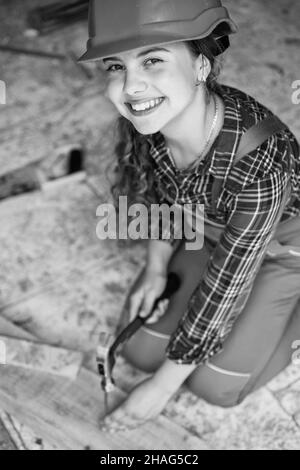 Portrait d'un enfant mignon posant comme un menuisier, avec un marteau. Travaillant comme menuisier. charpentier dans le travail de chapeau de protection. Fille travaillant avec le bois dans Banque D'Images