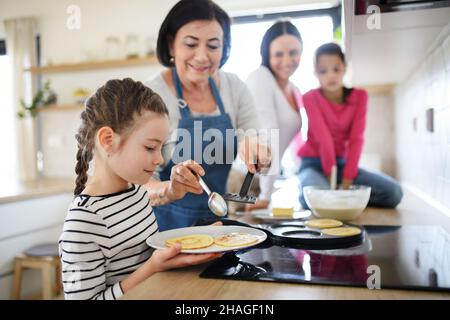 Petites filles heureuses avec la mère et la grand-mère faire des crêpes à l'intérieur à la maison, la cuisine. Banque D'Images