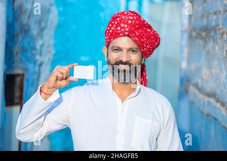 Jeune homme indien traditionnel montrant blanc blanc blanc carte de débit / crédit maquette, personne portant le turban rouge avec la barbe tenant des affaires vides ou élus Banque D'Images