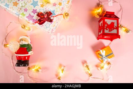 Fond de Noël - décorations de Noël - une guirlande, une boîte cadeau, une lampe de poche et un ours dans un costume de Père Noël sur un fond rose clair Banque D'Images
