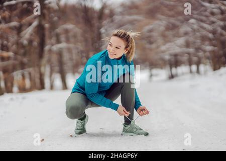 Sportswoman se bousculant sur la neige dans la nature en hiver et nouant le cordonnet.Baskets, fitness en hiver, vie saine, nature Banque D'Images