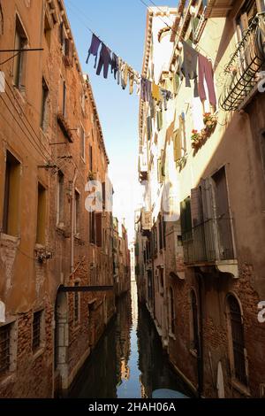 Un canal à Venise, en Italie, entre de vieux bâtiments avec des vêtements lavés des résidents accrochés entre eux, des rangées de fenêtres et des balcons Banque D'Images