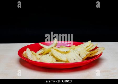 Gaufrettes de pommes de terre salées dans un plat rouge sur une table en bois, tas de gaufrettes, espace de copie, tas de frites, vue latérale,Isolé sur fond noir Banque D'Images