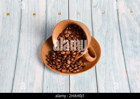 Une tasse et une soucoupe en céramique brune sont renversées et arrosées de grains de café.Une tasse se tient au milieu d'un fond en bois bleu Banque D'Images