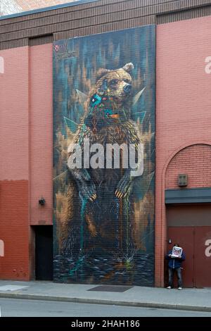 Sur la place Saint-Marc de Greenwich Village, un homme mange une pizza dans une boîte à côté d'une murale géante d'un ours. Banque D'Images