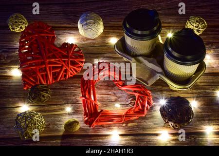Sur fond de bois, il y a deux tasses de café à droite et deux grands coeurs tissés décoratifs à gauche.Les lumières incandescentes sont éparpillées Banque D'Images