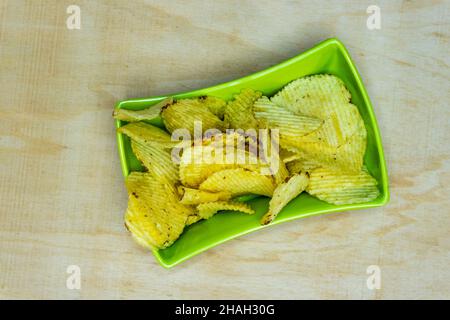 Gaufrettes de pommes de terre salées dans un bol carré vert sur une table en bois, tas de gaufrettes, espace de copie, tas de frites, vue de dessus Banque D'Images