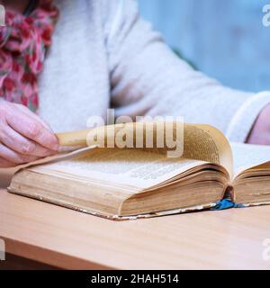 Une femme assise à une table lit et retourne à travers un livre. Mise au point sélective Banque D'Images