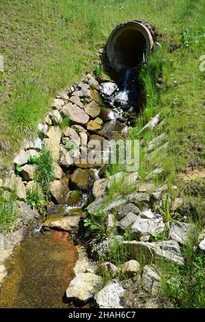 D'un grand tuyau en béton dans la colline, un ressort avec de l'eau propre coule et coule le long d'une gouttière spécialement couchée en pierres. Banque D'Images