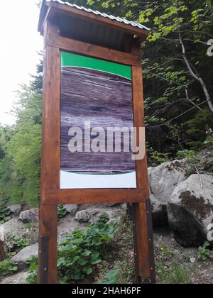 Dans la forêt, il y a un grand panneau en bois avec un espace vide pour l'insertion sur un fond de pierres. Banque D'Images