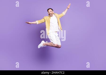 Photo de l'homme mûr très impressionné habillé jaune chemise verres sourire sautant haut isolé couleur violet fond Banque D'Images