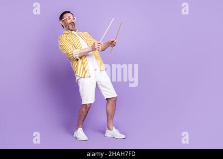 Photo de doux drôle mature homme habillé rayé chemise lunettes jouant tambours vide espace souriant isolé couleur violet fond Banque D'Images