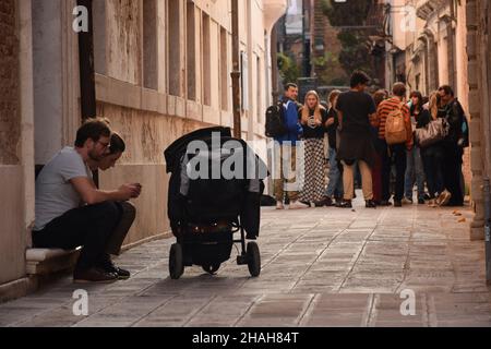 Dans la vieille ville, une famille avec une poussette est assise sur le trottoir.En arrière-plan, un groupe de jeunes Banque D'Images