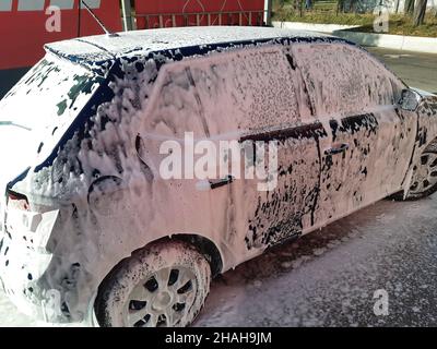 La voiture est bleu foncé, complètement recouverte de mousse blanche dans un lavage de voiture, préparé pour le lavage à l'eau Banque D'Images