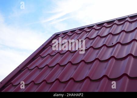 Partie d'un toit en métal ondulé rouge contre un ciel bleu.Il y a un espace vide sur la gauche pour insérer une étiquette Banque D'Images