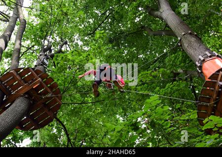 Un adolescent dans un harnais de sécurité traverse un pont suspendu dans un parc d'été à cordes Banque D'Images