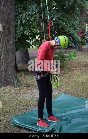 Un adolescent en équipement sportif pour grimper les arbres et les rochers déconnecte le mousqueton de l'équipement Banque D'Images