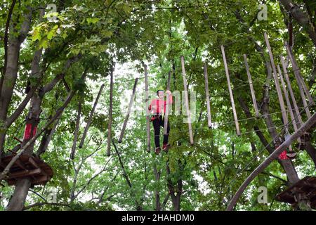 Un adolescent dans un harnais de sécurité traverse un pont suspendu dans un parc d'été à cordes Banque D'Images