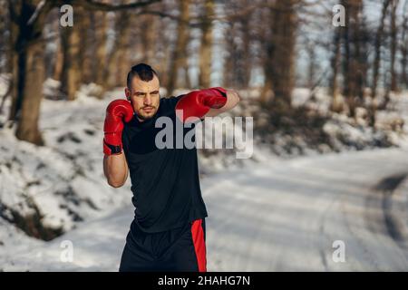 Boxeur robuste avec gants de boxe debout dans la nature lors d'un hiver enneigé et étincelant.Boxe dans la nature, vie saine, sport d'hiver Banque D'Images