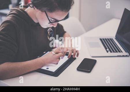 Dessin adolescent avec tablette et stylo virtuel.Étudiant du millénaire qui fait ses devoirs avec des appareils de nouvelle technologie.Un jeune garçon tire sur le coussin à la maison.Mains de sexe masculin Banque D'Images