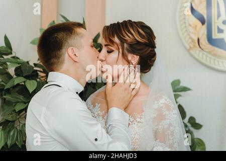 Mariage: Jeune couple en amour mariée et marié s'embrassant l'un l'autre tenant un bouquet de fleurs.Deux amants cœurs lors de la cérémonie de mariage.Élégant Banque D'Images