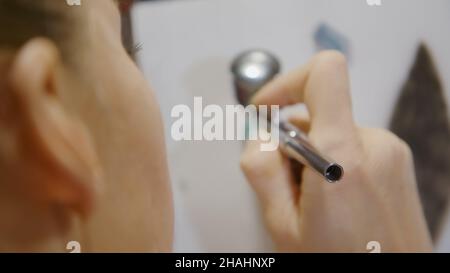 Une artiste apprend à peindre avec un aérographe avec du colorant acrylique, du papier et du chevalet.Concept art moderne, aérographe, aérographie, graffiti, aérosol Banque D'Images