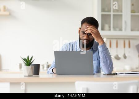 Triste fatigué malheureux malheureux déprimé millénaire afro-américain barbu mâle dans des lunettes travaillant sur ordinateur portable Banque D'Images