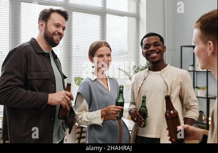 Groupe de jeunes collègues heureux avec des bouteilles de bière se parlant les uns aux autres pendant l'entreprise au bureau Banque D'Images