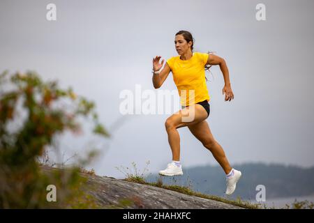 Femme de fitness concentrée qui fait de la course à haute intensité sur le flanc de montagne par le mer Banque D'Images