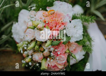 ANNEAUX D'OR DE MARIAGE ET BOUQUET DE FLEURS DE MARIÉE SUR FOND DE PIERRE.Bouquet de mariage blanc et rose de roses et paire d'anneaux de mariage dessus Banque D'Images