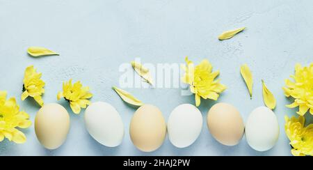 Concept de Pâques. Œufs et chrysanthèmes jaunes fleurs sur fond bleu. Maquette. Carte de vacances joyeuses Pâques du printemps. Vue de dessus. Banque D'Images