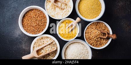 Variété de céréales flocons de riz, millet, sarrasin, flocons d'avoine.Superfood dans des bols en céramique blanche sur fond de vieux béton foncé.Vue de dessus. Banque D'Images