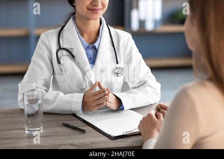 Bonne jeune femme indienne médecin en manteau blanc avec stéthoscope consulte le patient à l'intérieur de la clinique de bureau Banque D'Images