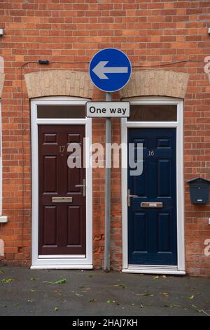 Rue à sens unique, deux portes, portes avant, 16/17, flèche à sens unique,chemin de pied, porte marron, porte bleue, bâtiment en brique, boîtes aux lettres,signe entre deux portes. Banque D'Images