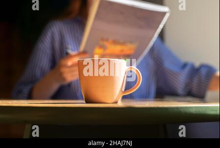 Tasse de café sur table en bois dans le café, mains de femmes floues avec un carnet de texte ou un carnet, lecture et écriture, préparation à l'examen avec bloc-notes ou planificateur de gros plan. Banque D'Images