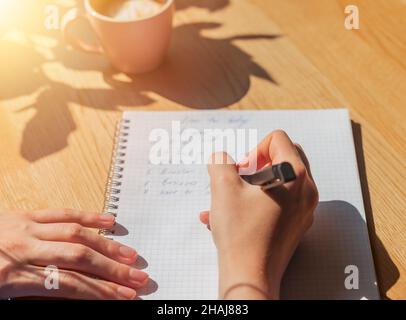 Les femmes écrivent des plans dans un carnet ou un planificateur sur une table de café en bois avec lumière du soleil de la fenêtre . Banque D'Images