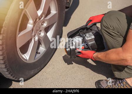 Les mains des hommes dans les gants et la pompe à pneus portative pour gonfler la roue automatique.Compresseur de gonflage de pneus avec manomètre. Banque D'Images