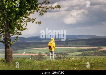 Femme debout au vent pendant la randonnée au printemps.Tempête et pluie arrivent.Tourist porte une veste imperméable avec capuche Banque D'Images