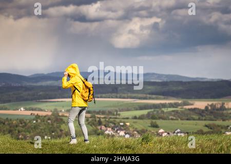 Tempête et pluie arrivent.Tourist porte une veste imperméable avec capuche.Femme randonnée dans un paysage rural au printemps Banque D'Images