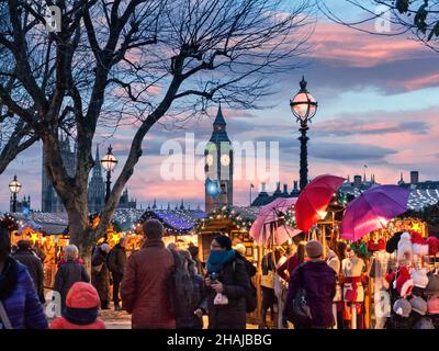 ÉTALS DU MARCHÉ DE NOËL D'HIVER DE LONDRES SOUTH BANK SHOPPERS LUMIÈRES WESTMINSTER South Bank marché de Noël Stals et shoppers avec des chambres du Parlement derrière au crépuscule coucher du soleil Londres Royaume-Uni Banque D'Images