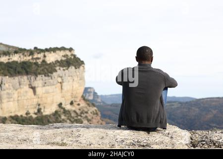 Vue arrière portrait d'un homme à la peau noire assis dans la nature contemplant des vues Banque D'Images